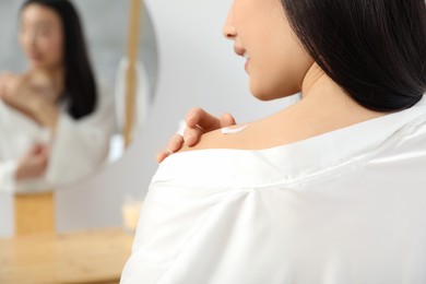 Photo of Young woman applying body cream on shoulder in room, closeup. Space for text