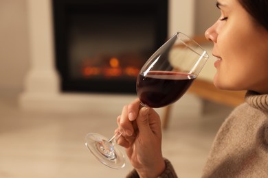 Photo of Young woman with glass of wine relaxing near fireplace at home, closeup. Space for text