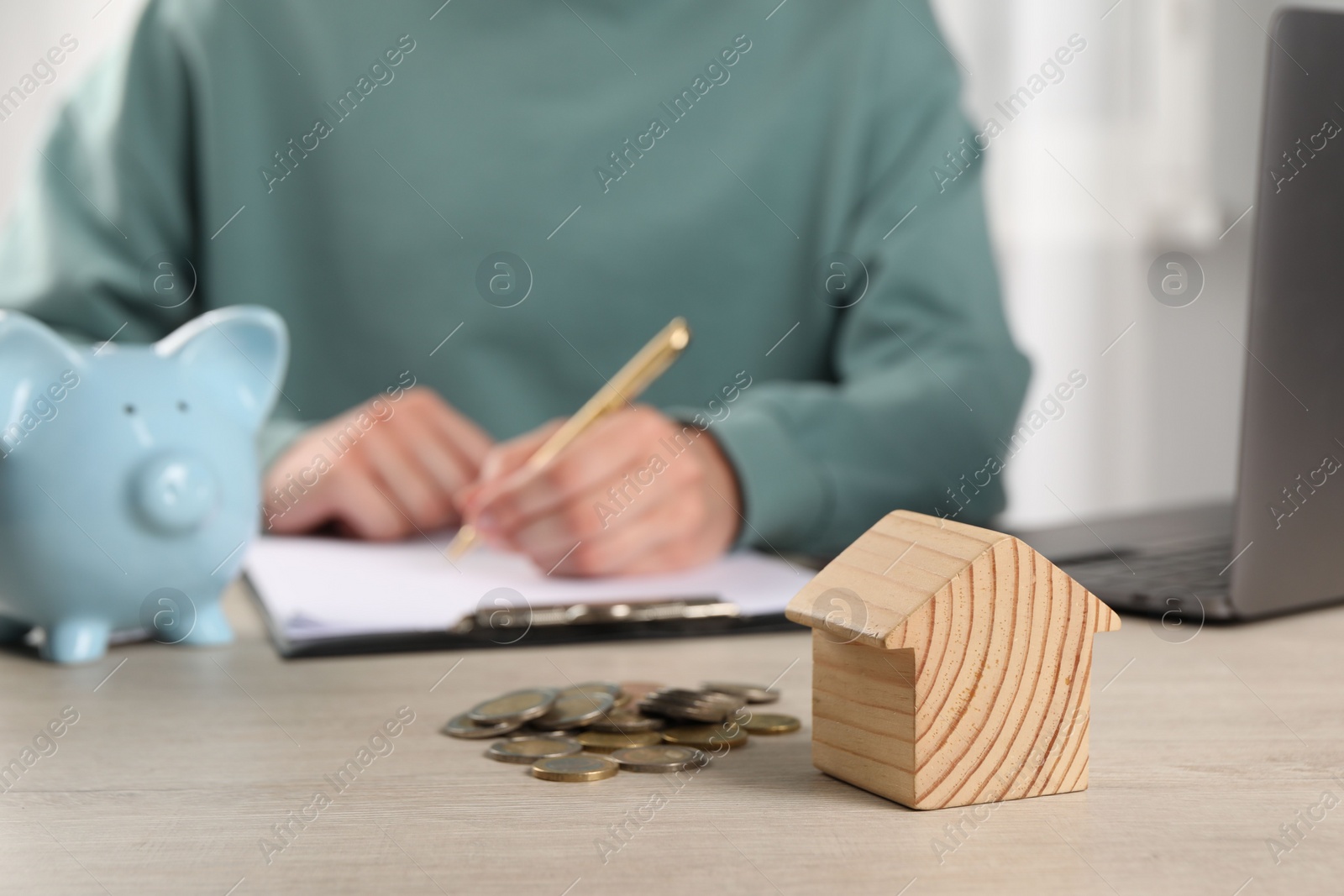 Photo of Woman planning budget at wooden table, focus on house model and coins