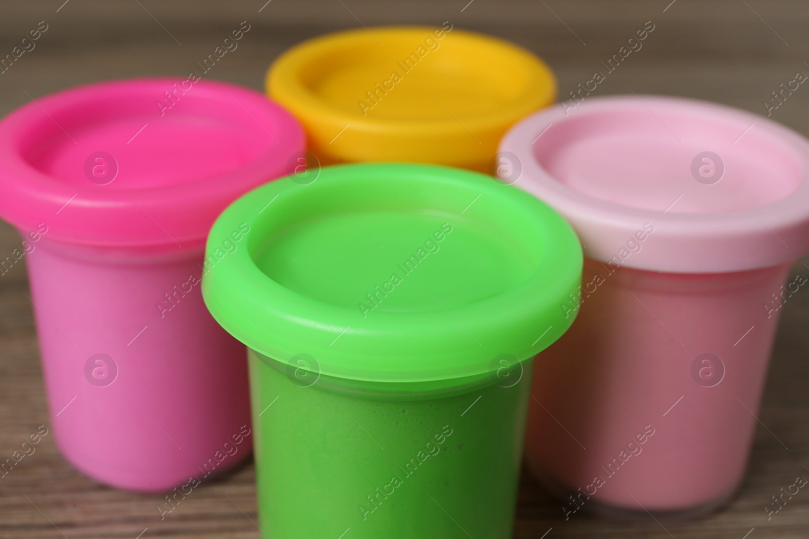 Photo of Plastic containers with colorful play dough on wooden table, closeup