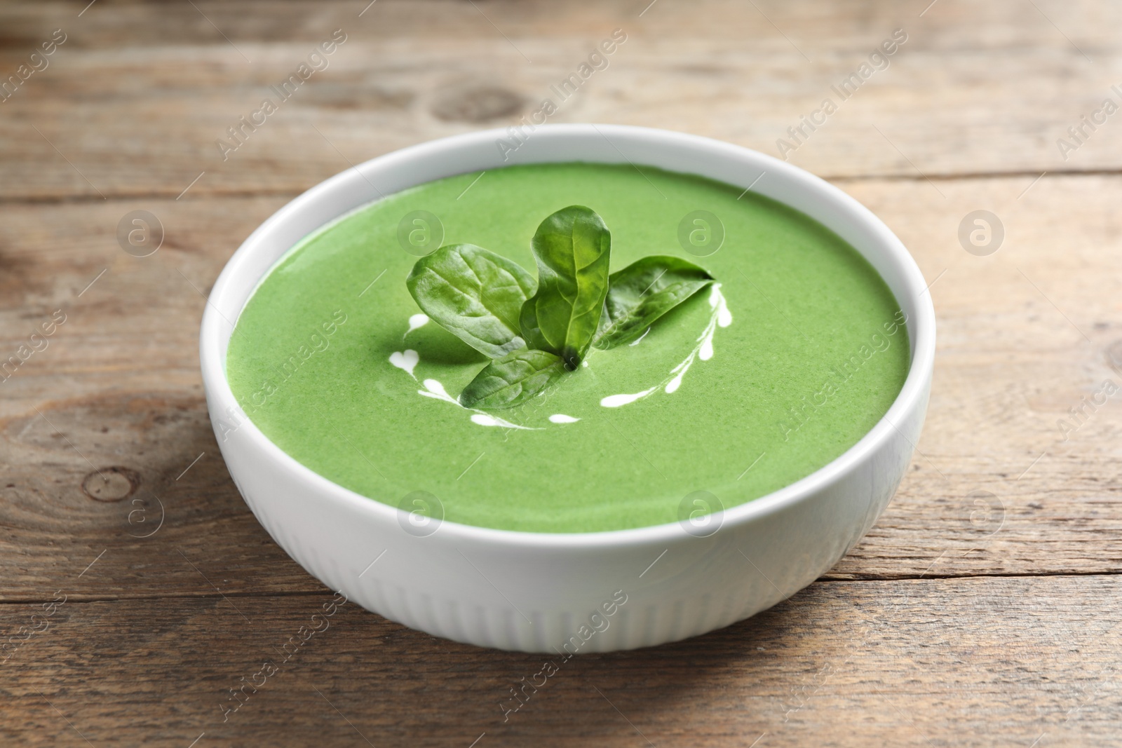 Photo of Bowl of healthy green soup with fresh spinach on wooden table