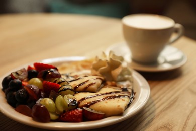 Delicious pancake with fresh fruits and cup of aromatic coffee on wooden table, closeup