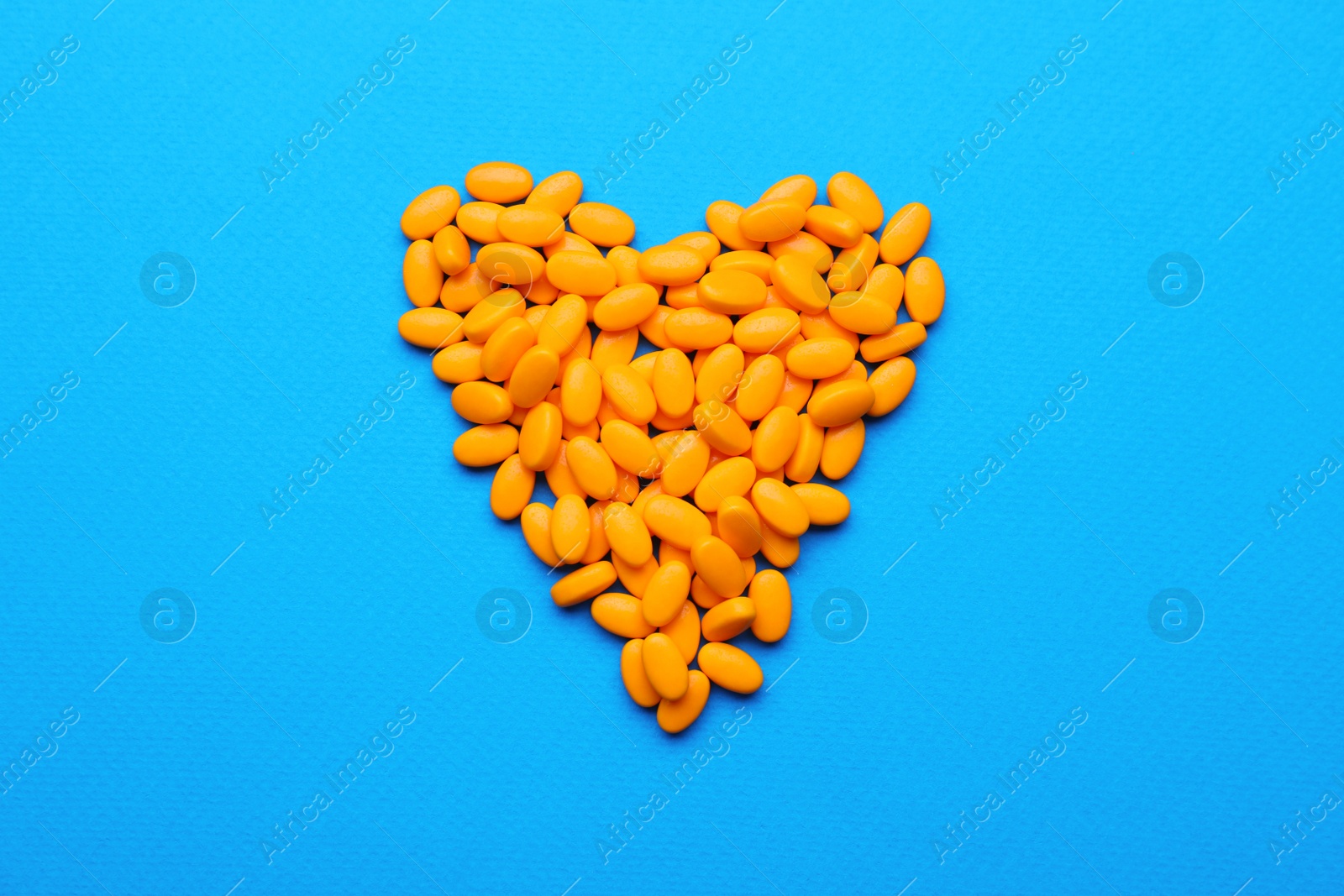 Photo of Heart made of orange dragee candies on blue background, flat lay