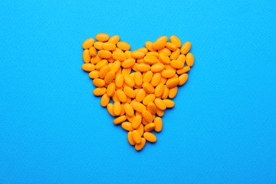 Photo of Heart made of orange dragee candies on blue background, flat lay
