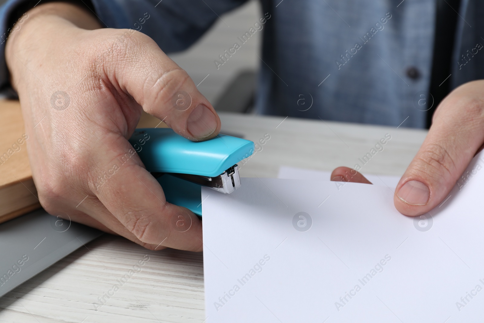 Photo of Man with papers using stapler at white table, closeup