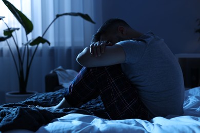 Tired man sitting on bed at night