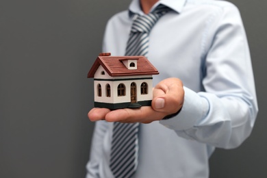 Photo of Real estate agent holding house model on gray background