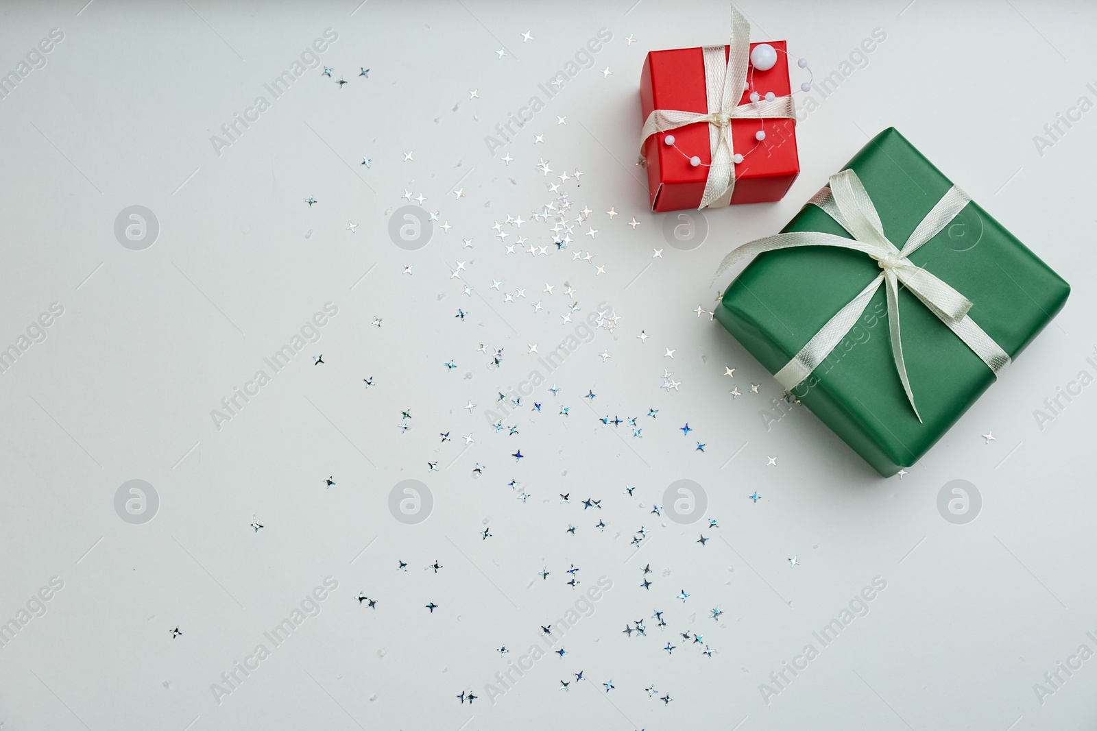 Photo of Christmas gift boxes with shiny confetti on light background, flat lay. Space for text