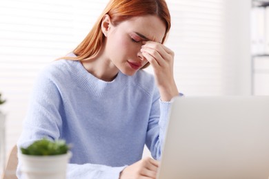 Photo of Woman suffering from headache at workplace indoors