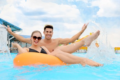 Happy couple with inflatable ring in swimming pool at water park