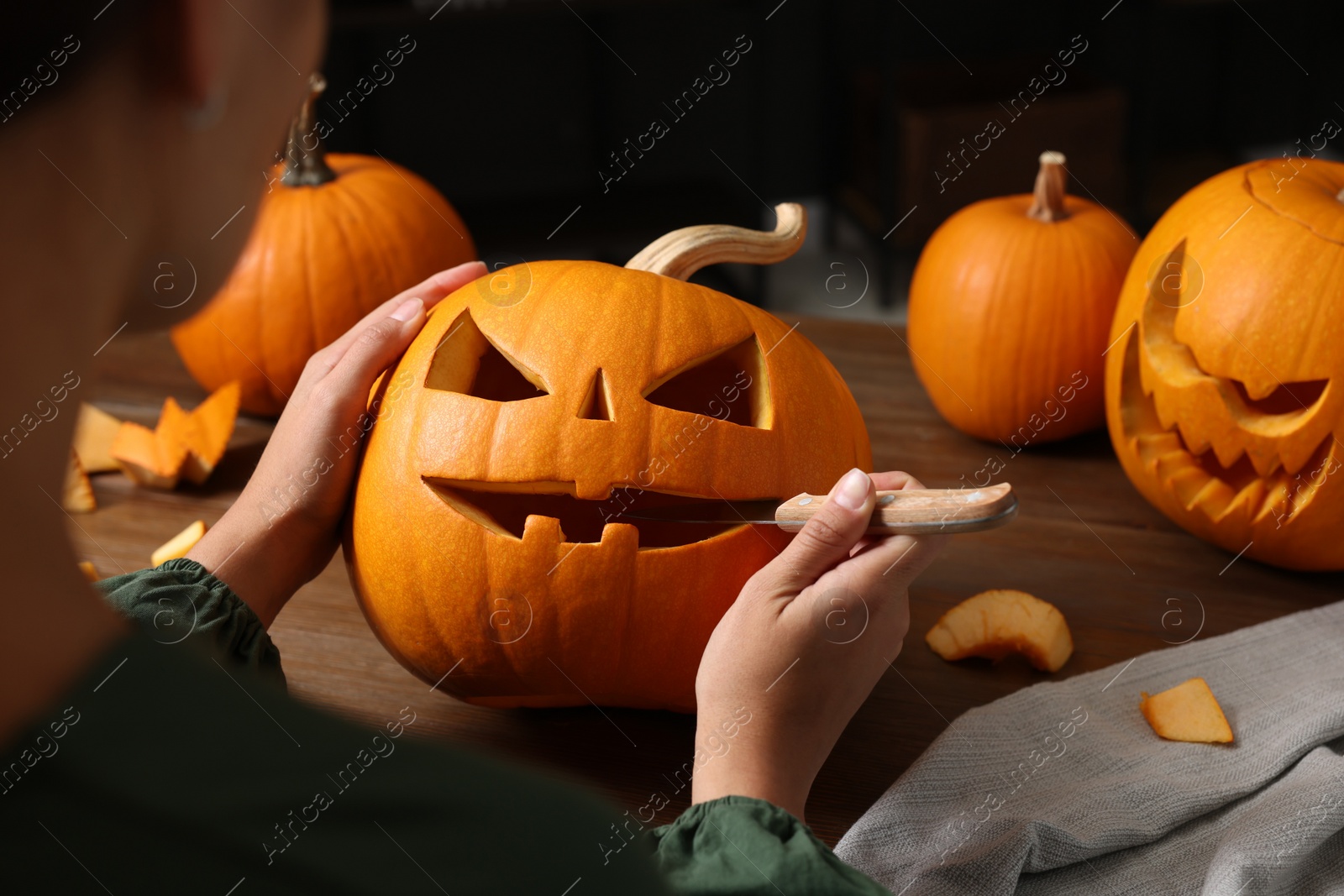 Photo of Woman carving pumpkin for Halloween at wooden table, closeup