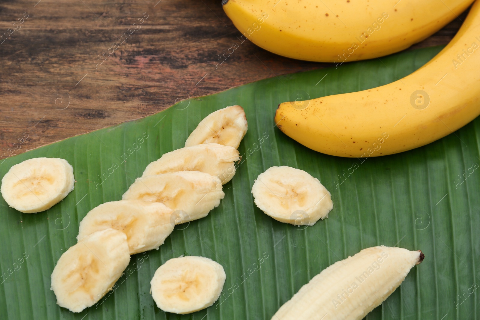 Photo of Delicious ripe bananas and fresh leaf on wooden table, above view