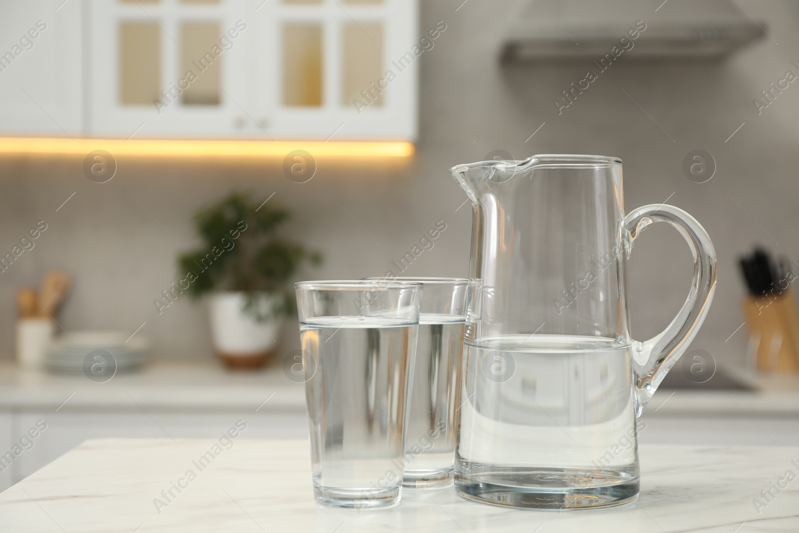 Photo of Jug and glasses with clear water on white table in kitchen, space for text