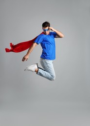 Photo of Man in superhero cape and mask jumping on grey background