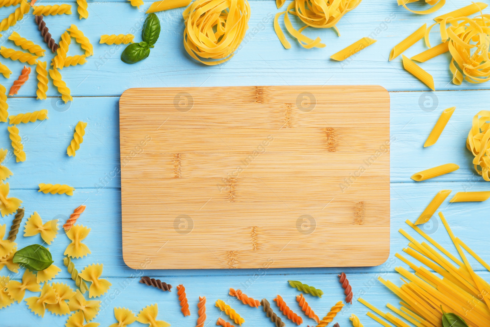 Photo of Wooden board and different raw pasta on table, top view