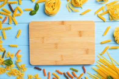 Wooden board and different raw pasta on table, top view