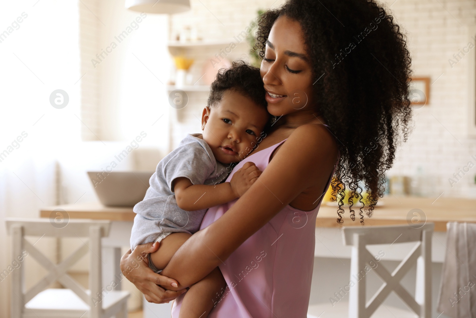 Photo of African-American woman with her baby in kitchen. Happiness of motherhood