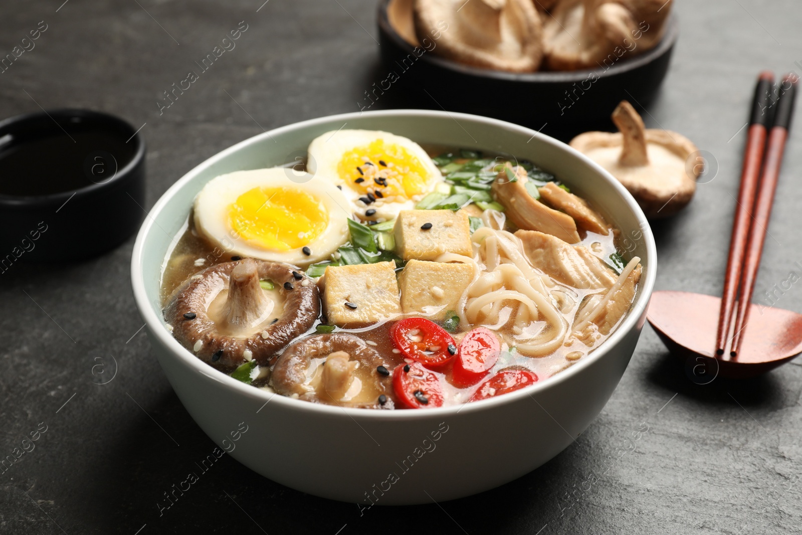 Photo of Noodle soup. Bowl of delicious ramen, ingredients and chopsticks on black table, closeup