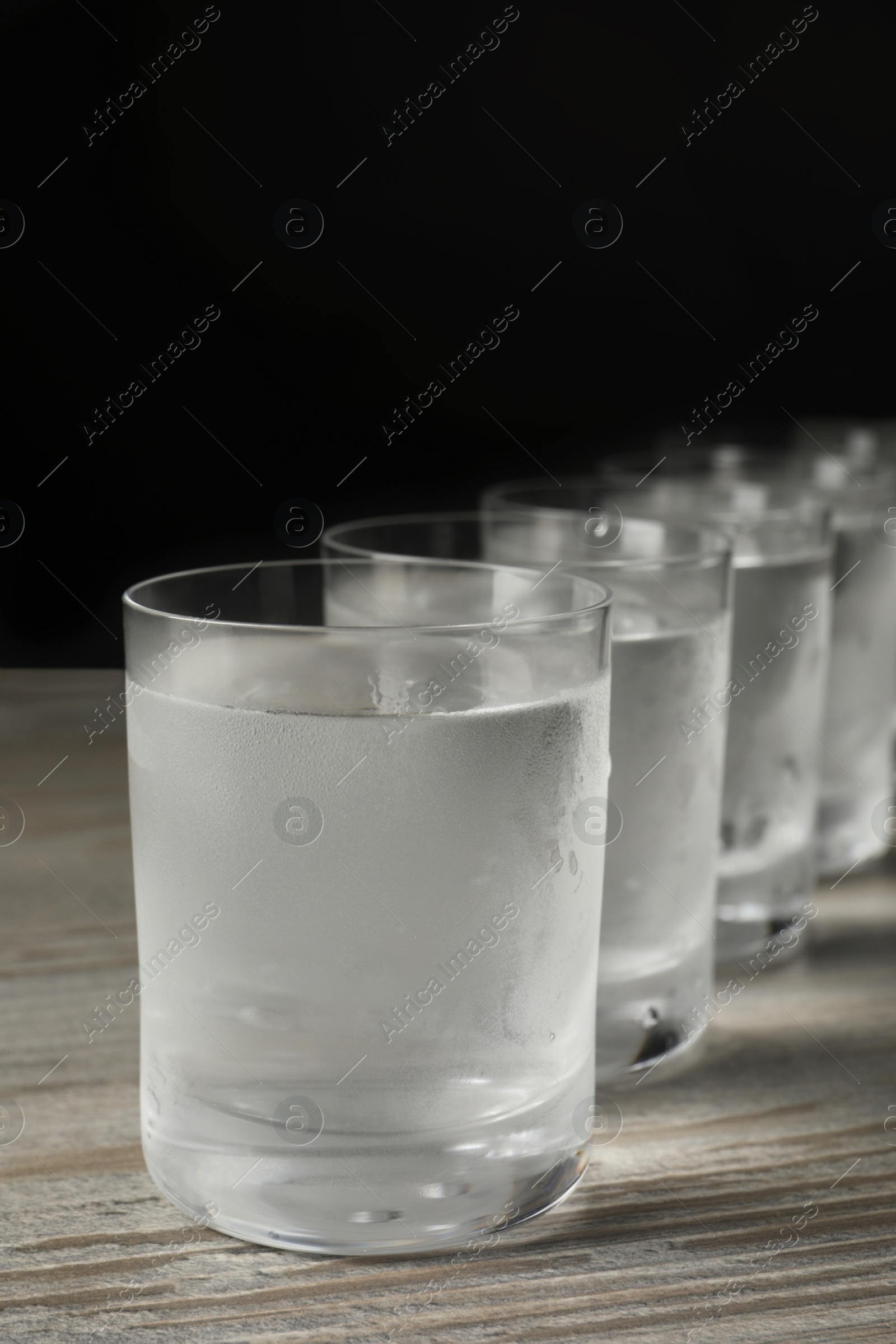 Photo of Shot glasses of cold vodka on wooden table against grey background, closeup