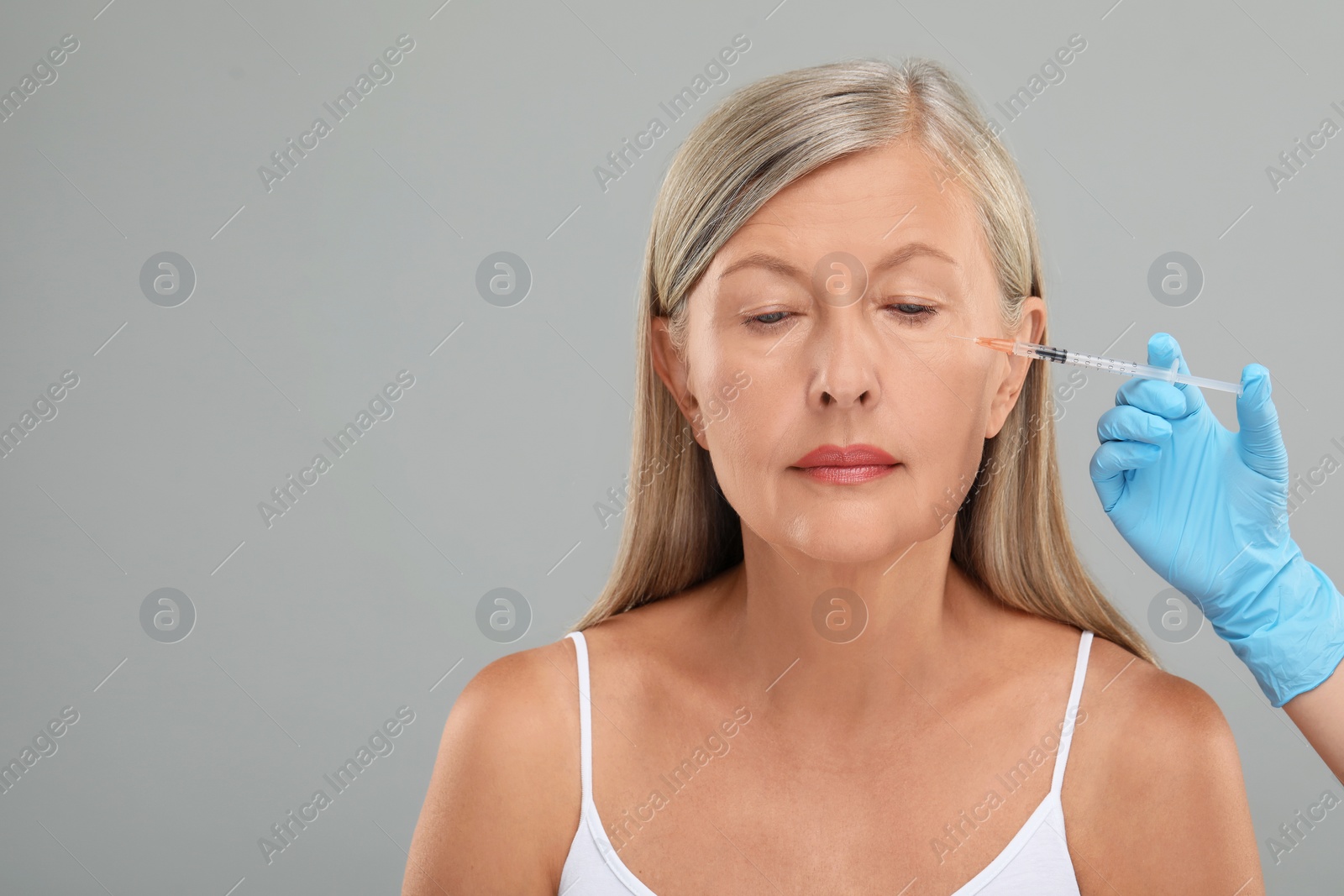 Photo of Doctor giving facial injection to senior woman on light grey background, closeup and space for text. Cosmetic surgery