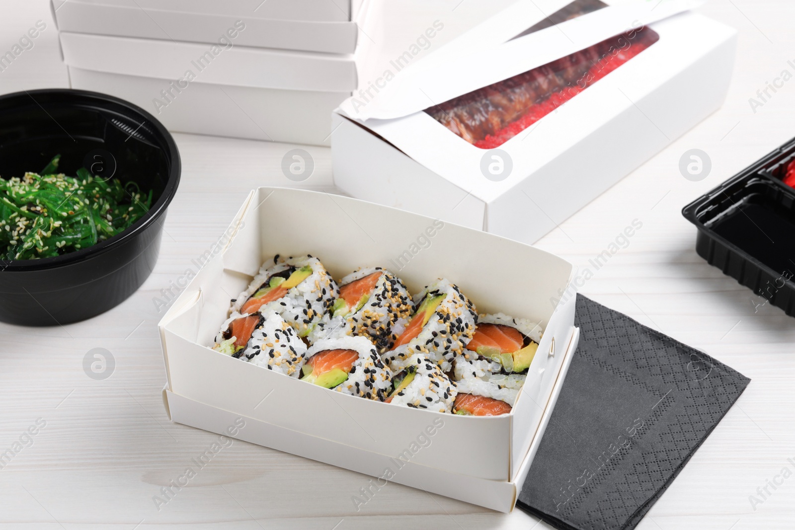 Photo of Food delivery. Paper boxes with delicious sushi rolls on white wooden table