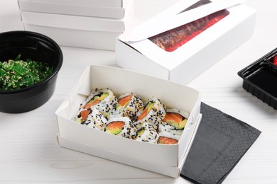 Food delivery. Paper boxes with delicious sushi rolls on white wooden table