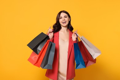 Beautiful young woman with paper shopping bags on yellow background