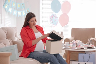 Photo of Happy pregnant woman with gift box in room decorated for baby shower party
