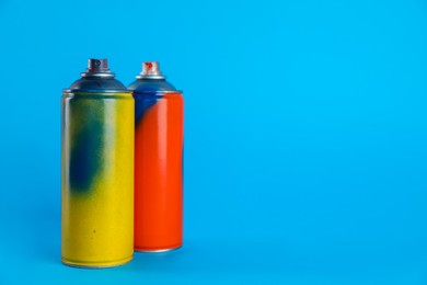 Photo of Used cans of spray paints on light blue background. Space for text