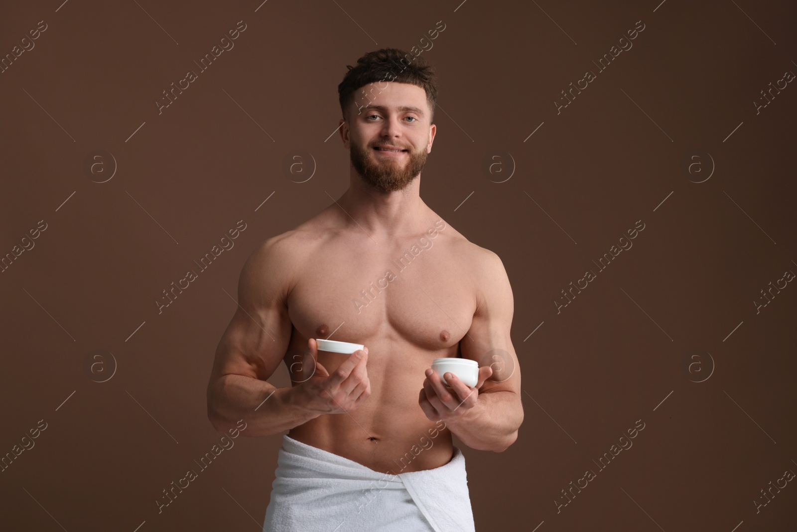 Photo of Handsome man holding jar with moisturizing cream on brown background