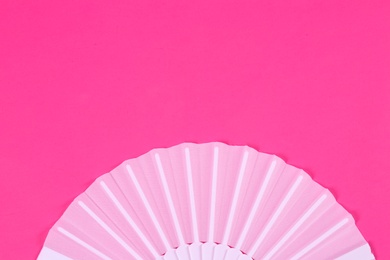 White hand fan on pink background, top view. Space for text