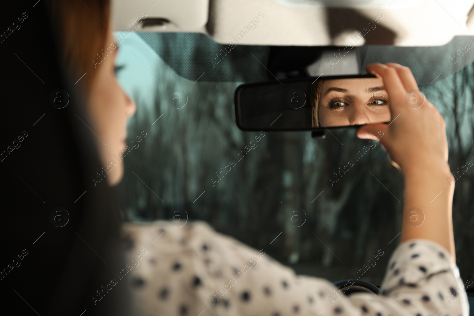 Photo of Young woman adjusting rear view mirror in car, closeup