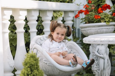 Photo of Cute little girl in white dress sitting in chair outdoors