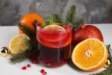Christmas Sangria drink in glass, fir branches and fruits on white table, closeup