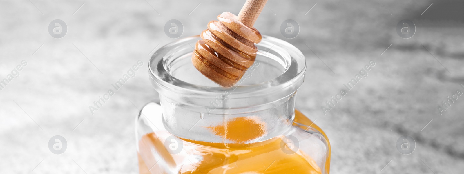 Image of Dripping tasty honey from dipper into glass on table, closeup. Banner design