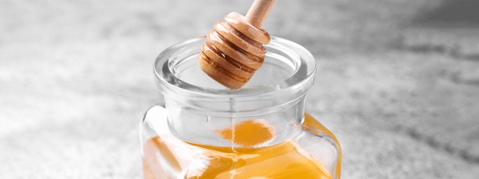 Image of Dripping tasty honey from dipper into glass on table, closeup. Banner design