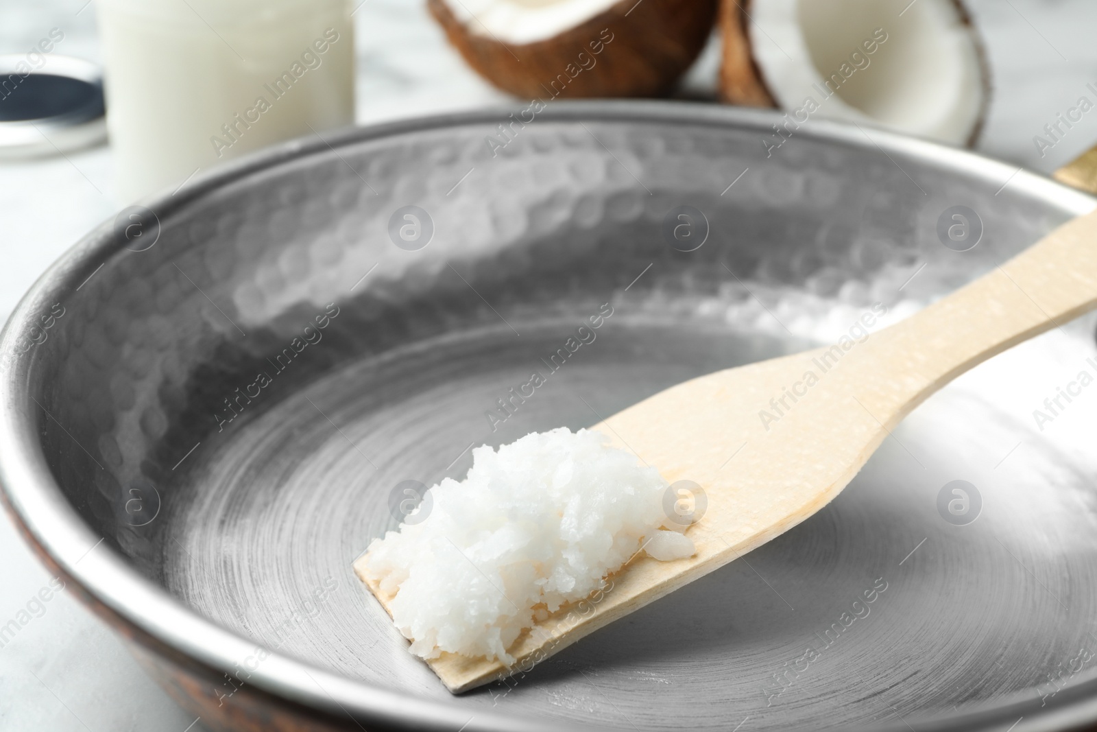 Photo of Frying pan with coconut oil and wooden spatula on white marble table, closeup. Healthy cooking