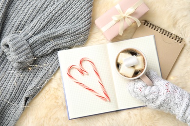 Woman holding cup of hot winter drink on notebook, top view. Cozy season