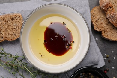 Photo of Bowl of organic balsamic vinegar with oil, spices and bread slices on grey table, flat lay