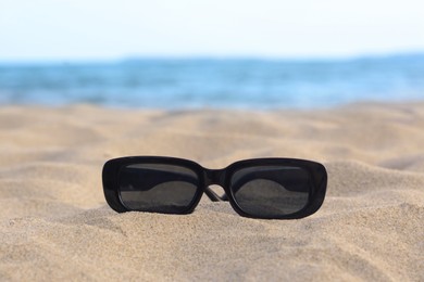 Stylish sunglasses on sandy beach near sea, closeup. Space for text