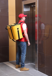 Photo of Male courier with thermo bag waiting for elevator. Food delivery service