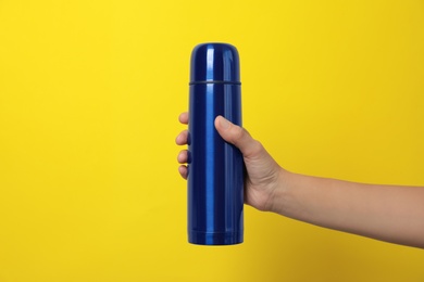 Photo of Woman holding modern blue thermos on yellow background, closeup