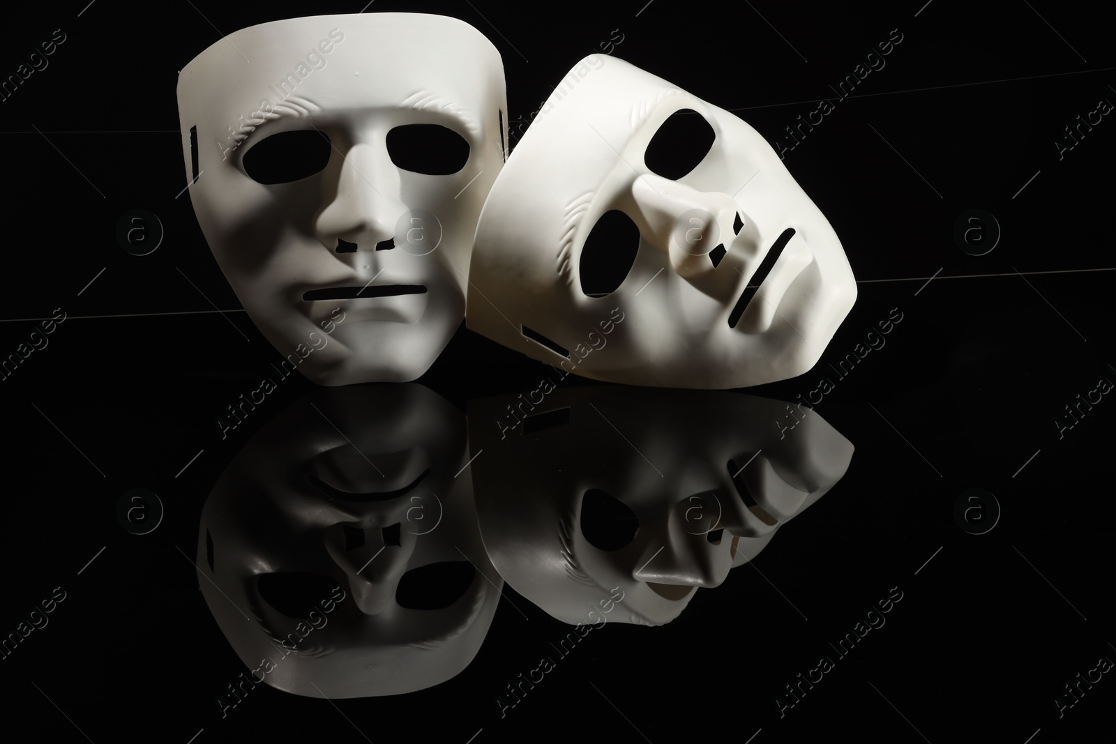 Photo of Plastic face masks on black mirror surface, space for text. Theatrical performance