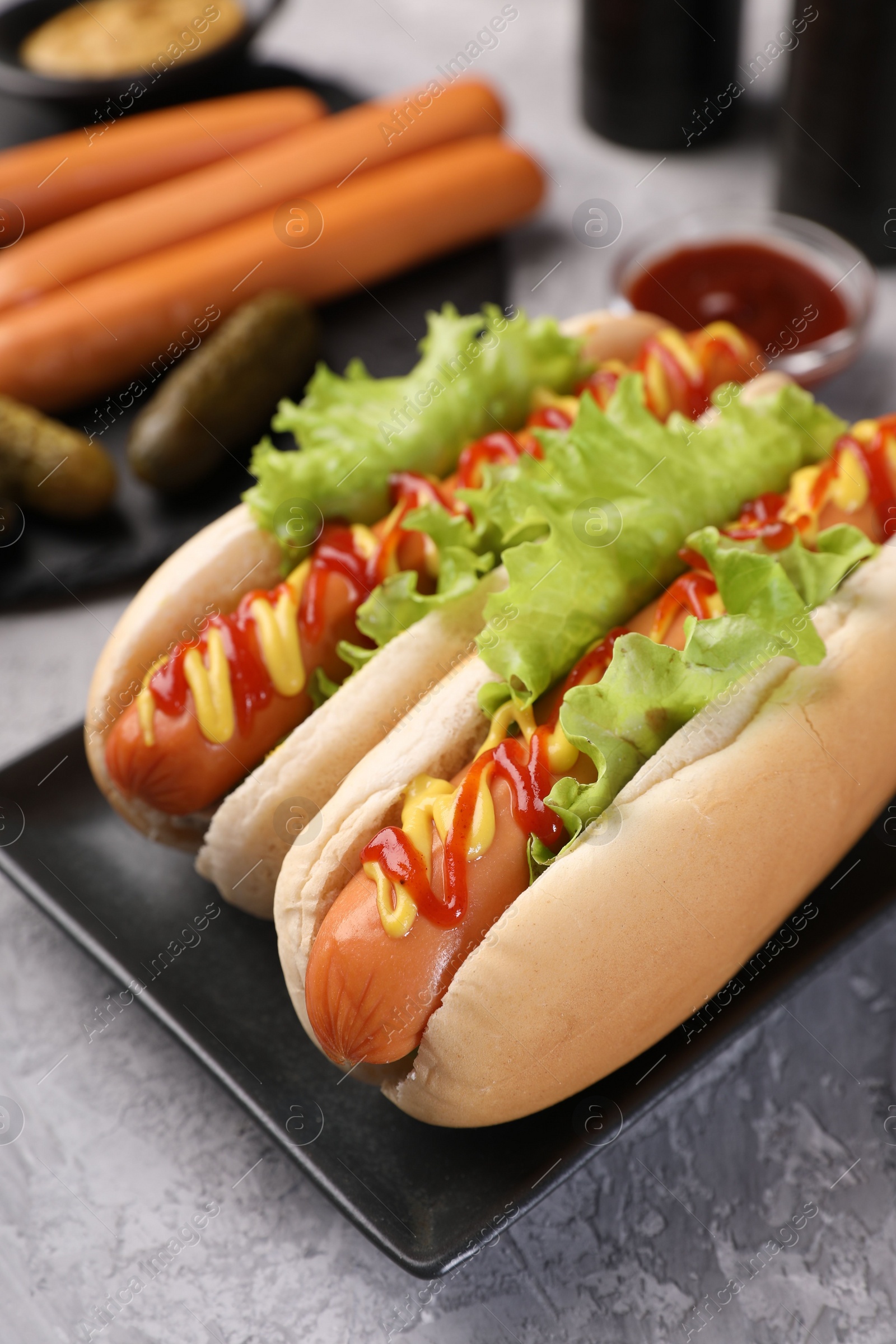 Photo of Tasty hot dogs with lettuce, ketchup and mustard on grey textured table, closeup