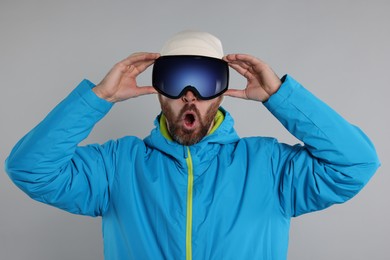 Photo of Winter sports. Emotional man in ski suit and goggles on gray background