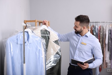 Photo of Dry-cleaning service. Worker holding hanger with coat in plastic bag indoors