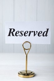 Photo of Elegant sign RESERVED on white wooden surface. Table setting element