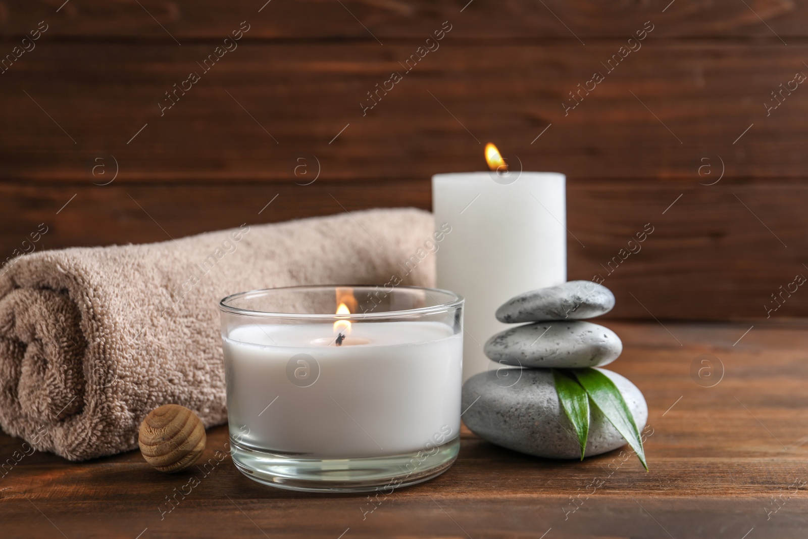 Photo of Beautiful composition with spa stones, towel and burning candles on wooden table