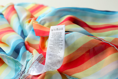 Photo of Clothing label with care instructions on colorful striped garment, closeup