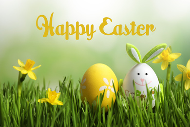 Image of Colorful eggs with narcissus flowers in green grass and text Happy Easter against blurred background